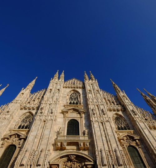 A stunning low angle view of Milan Cathedral's gothic architecture under a clear blue sky.